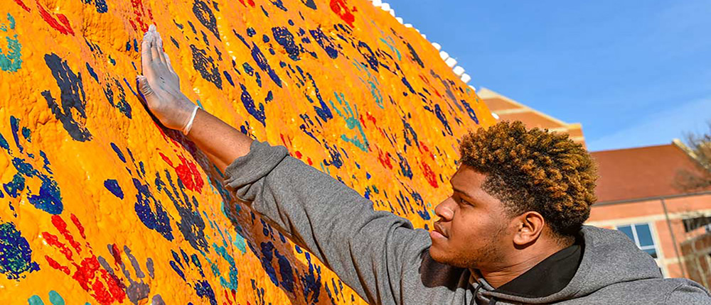 Male student applying a handprint to the Rocky Top rock.